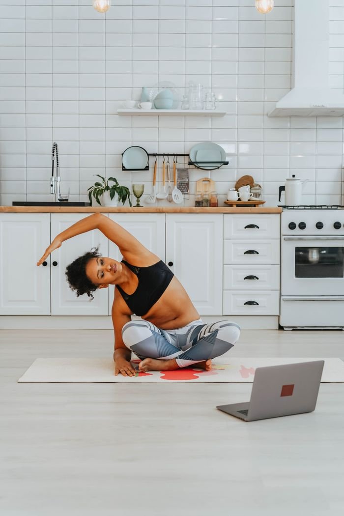 A woman exercises with online yoga videos in her stylish kitchen.